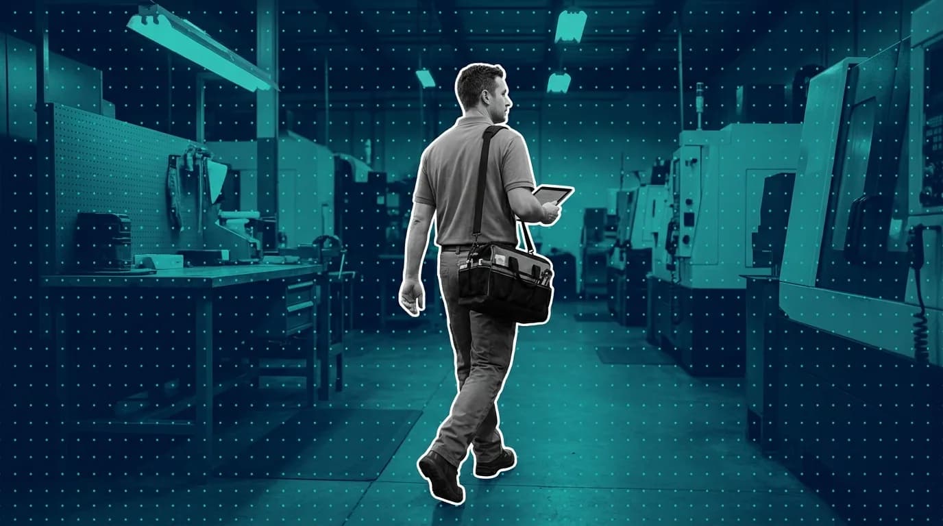 Maintenance technician walking a machine shop aisle with a tool bag over one shoulder and a tablet in hand